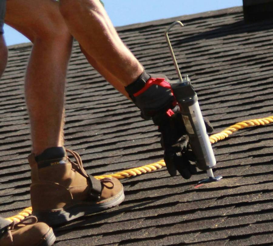 Gloved hand applying sealant to a shingle fastener