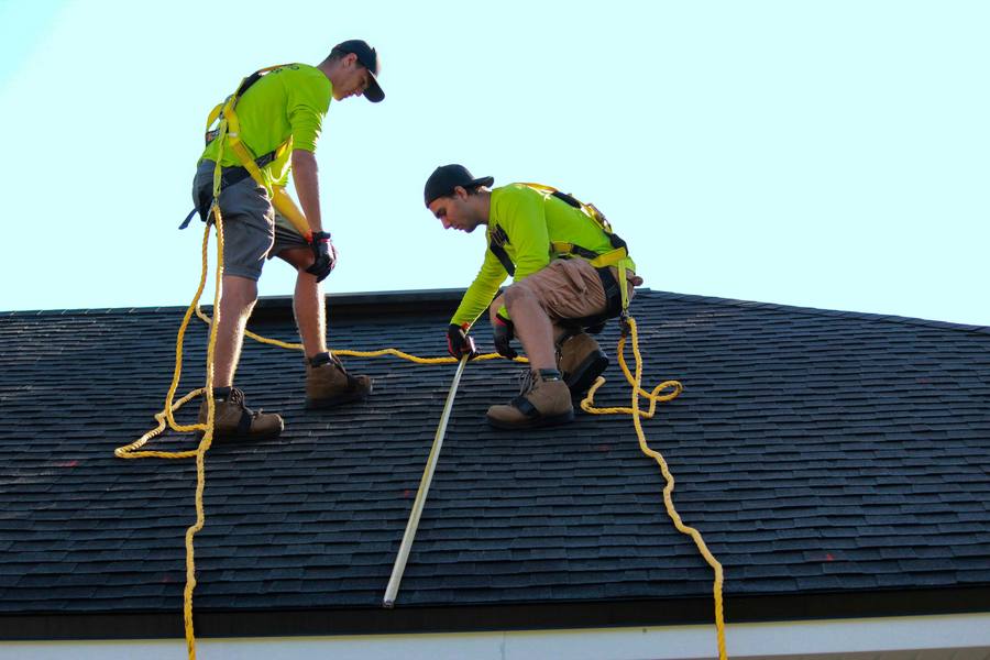 Two roofers in safety harnesses measuring an asphalt shingle roof