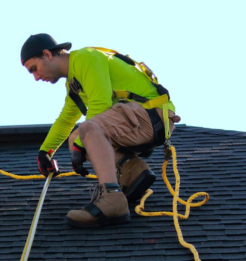 Roofer crouching to take a measurement with a tape