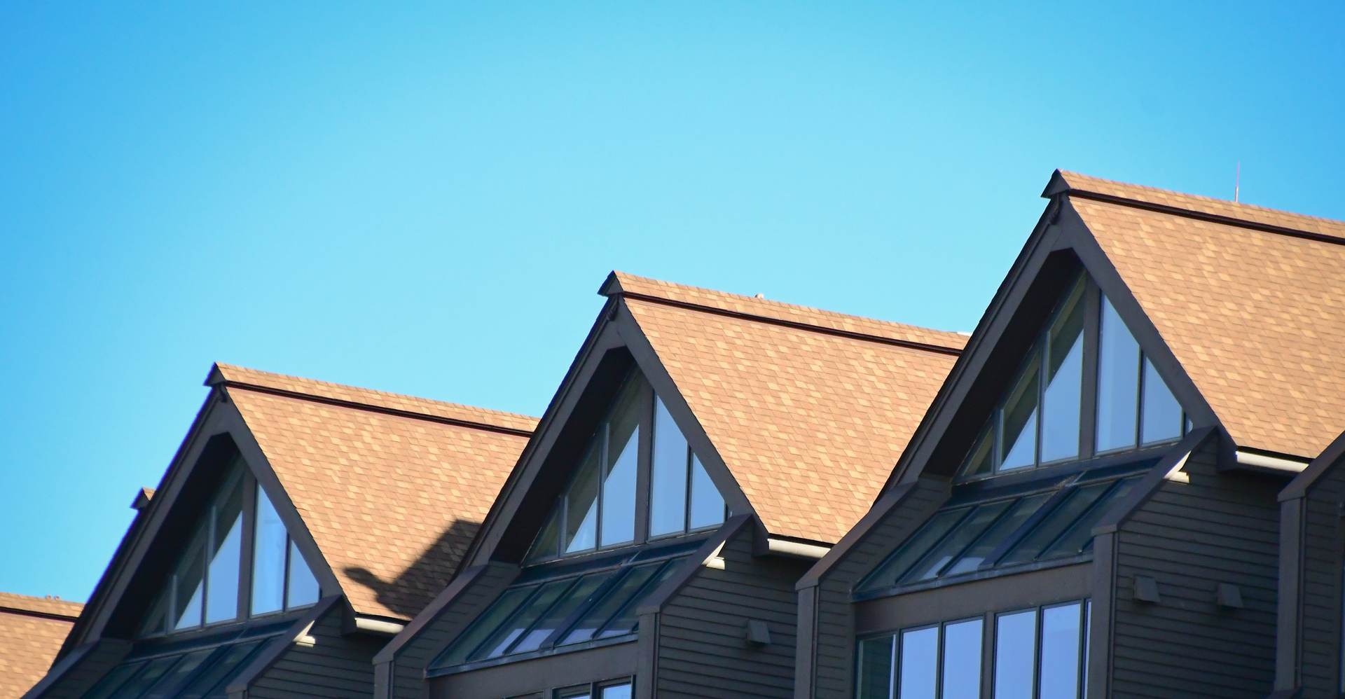 Tan shingle roofs on gabled dormers against a clear blue sky